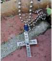 Words stamped on silver cross necklace on brick