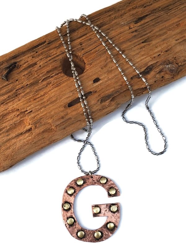 mixed metal letter g necklace on wood